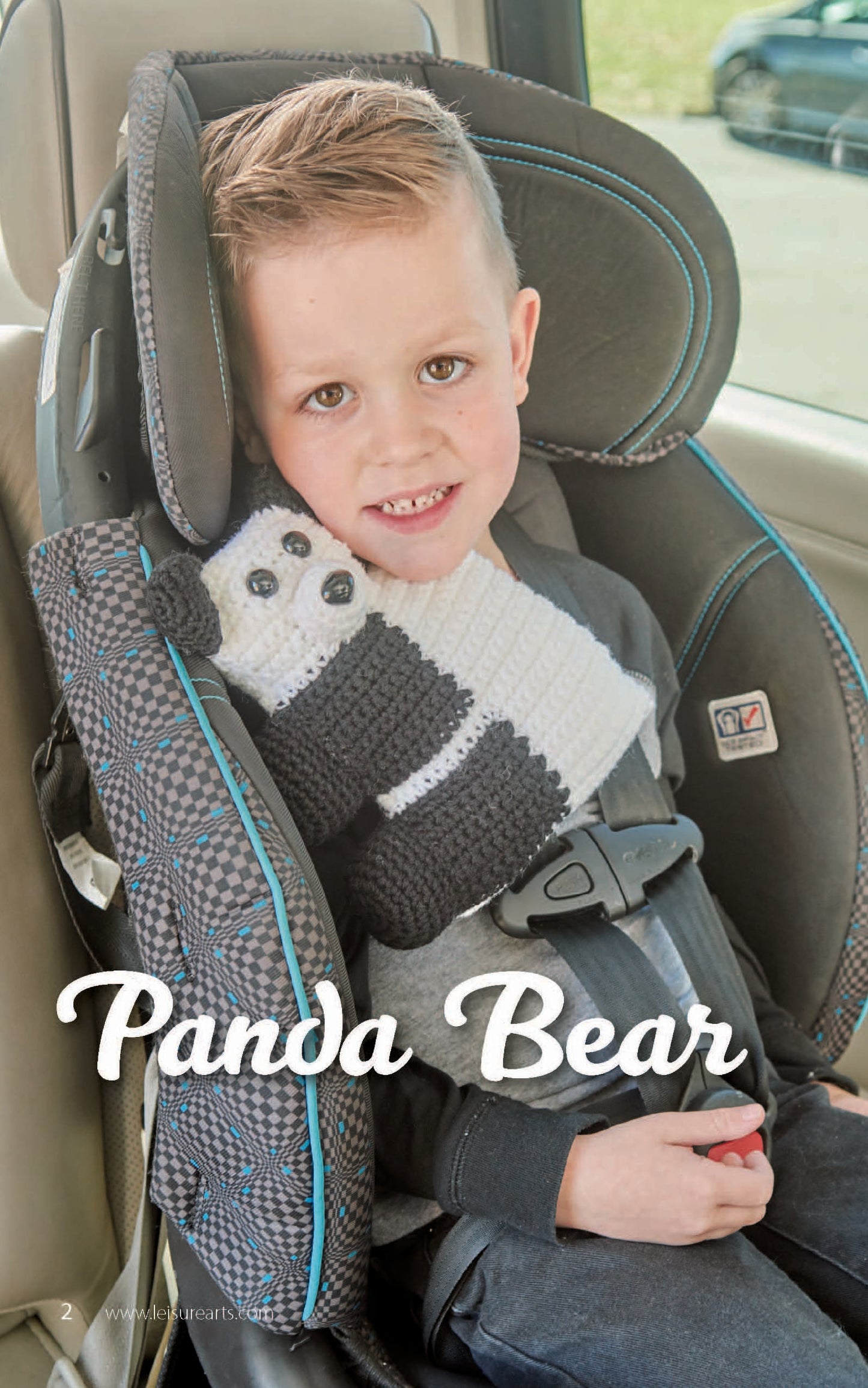 A young boy smiles in a car seat, buckled in with a Leisure Arts Car Seat Cuties panda bear cover—ideal for crochet animal lovers. "Panda Bear" is written on the image.