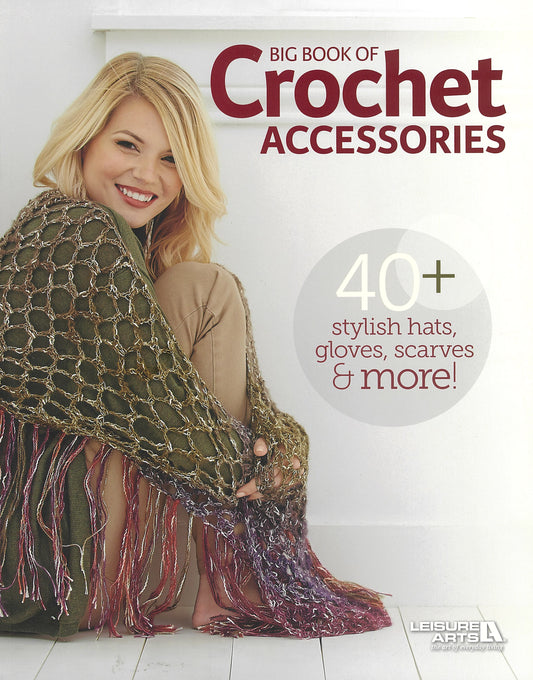 A smiling woman sits on the floor wearing a chunky crocheted shawl, surrounded by hats, scarves, and gloves. The cover reads “Big Book of Crochet Accessories” by Leisure Arts: 40+ stylish hats, gloves, scarves & more!.