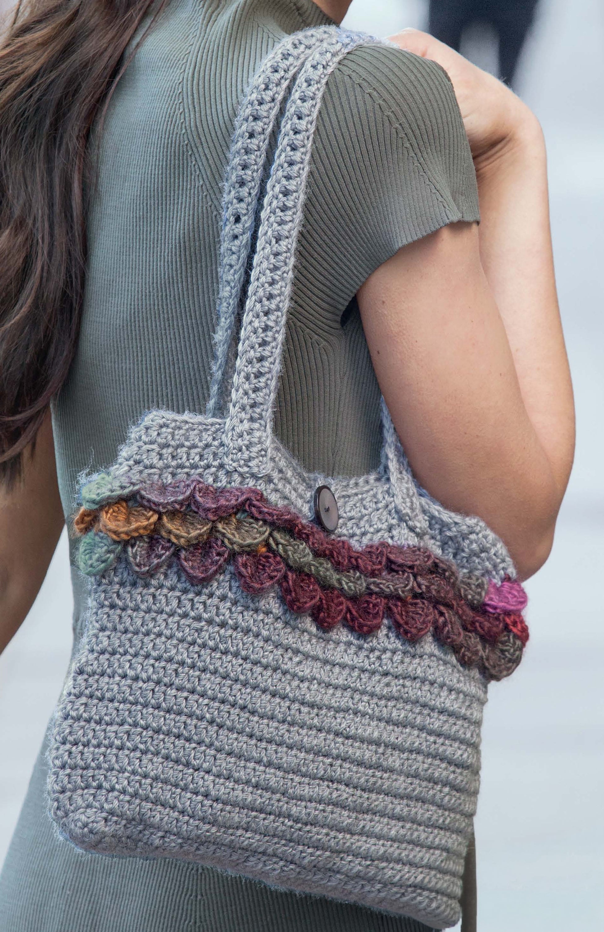 A person carries a gray crocheted handbag with colorful trim, made using patterns from Leisure Arts' Big Book of Crochet Accessories—perfect for pairing with hats or scarves to create a chic ensemble.