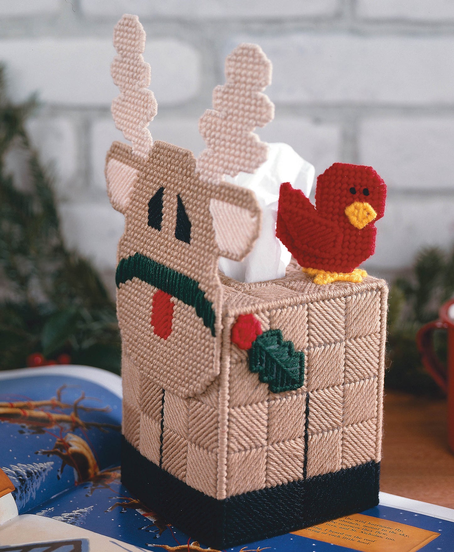 The Magic of Christmas by Leisure Arts offers 37 festive plastic canvas projects, including a yarn tissue box cover featuring a reindeer with antlers and a red bird—ideal for your holiday décor and creative Christmas displays.