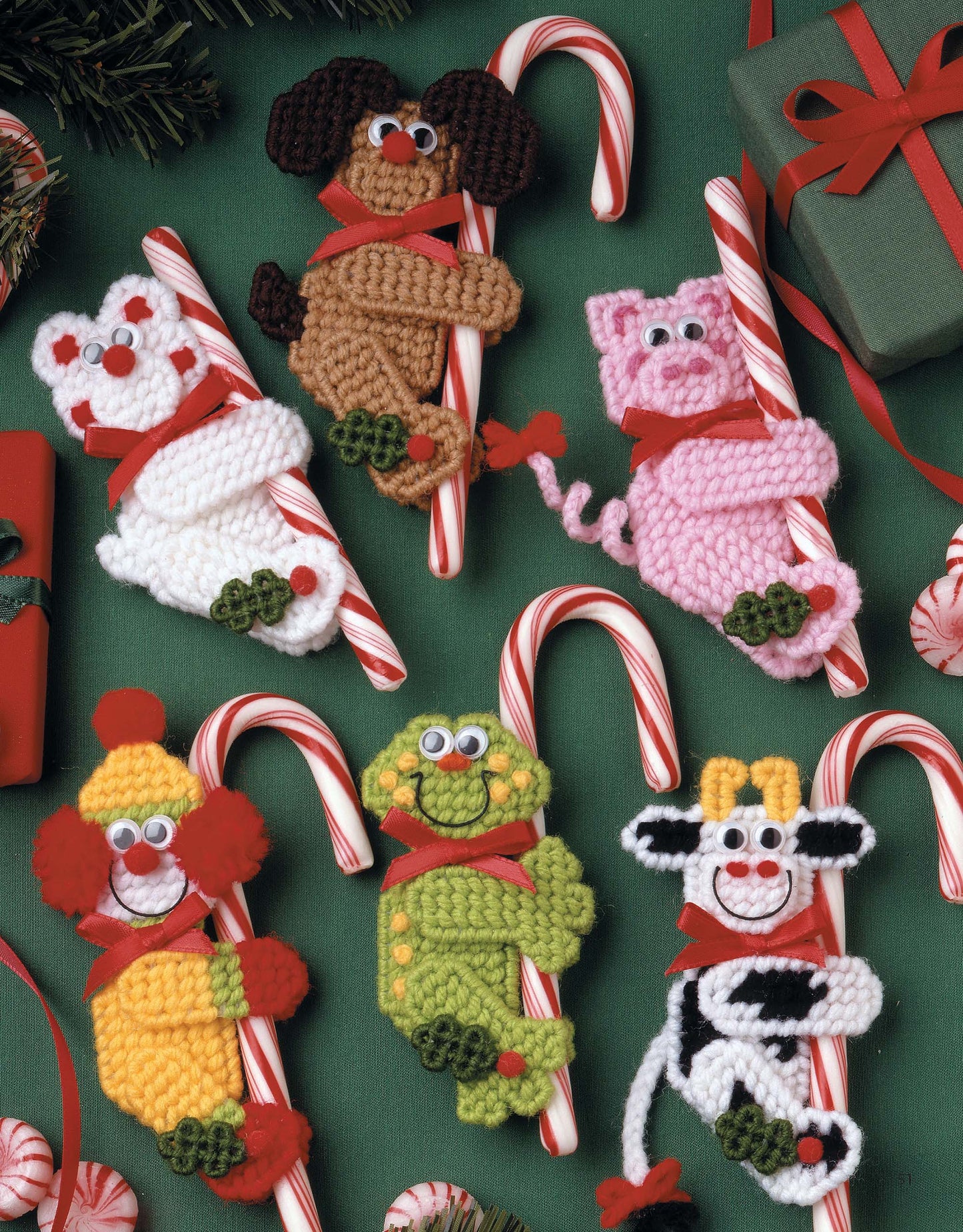 Six crocheted animal ornaments hugging candy canes, surrounded by gifts and peppermint candies, inspire festive creations in Leisure Arts' "The Magic of Christmas—37 Holiday Plastic Canvas Projects" craft book.