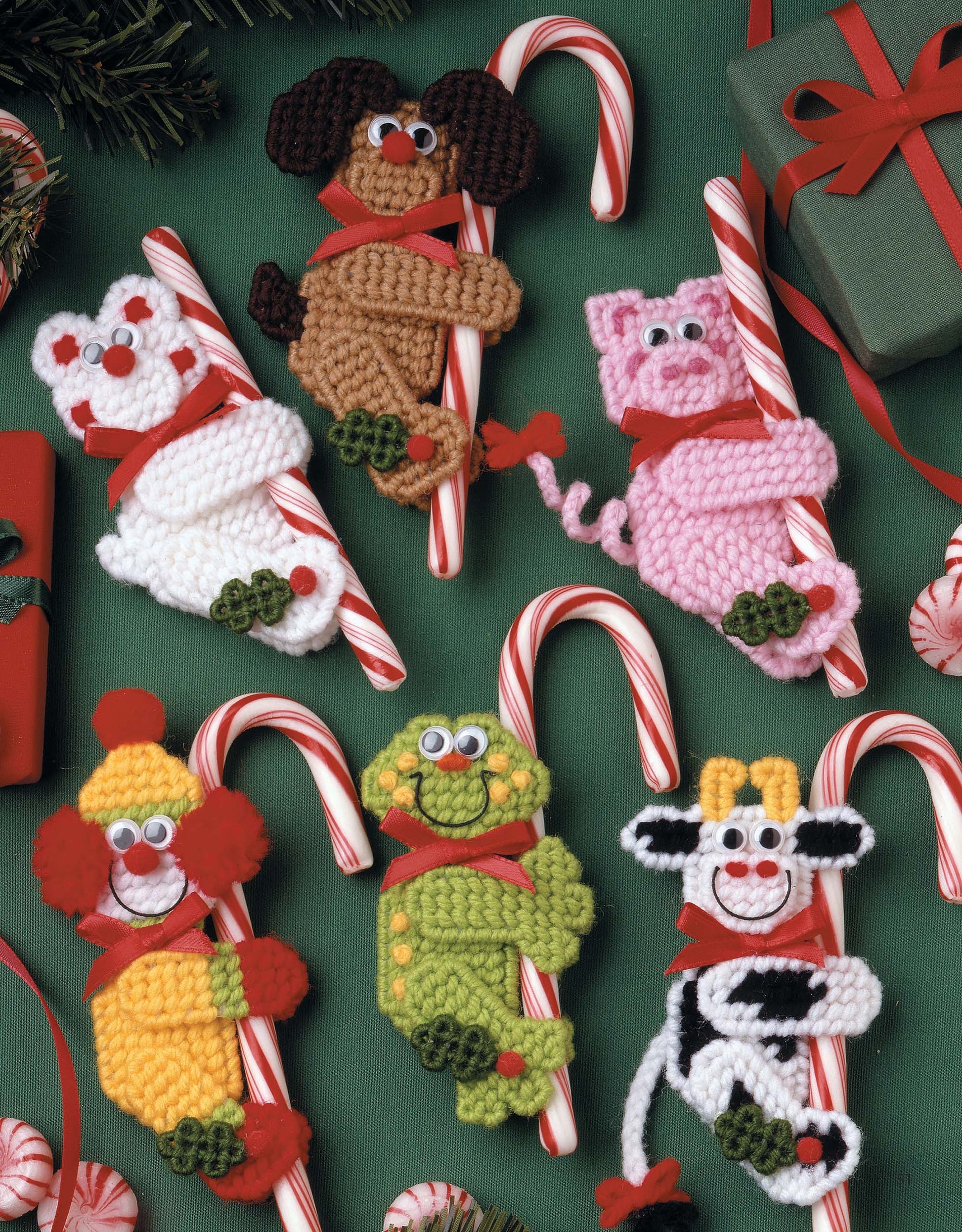 Six crocheted animal ornaments hugging candy canes, surrounded by gifts and peppermint candies, inspire festive creations in Leisure Arts' "The Magic of Christmas—37 Holiday Plastic Canvas Projects" craft book.
