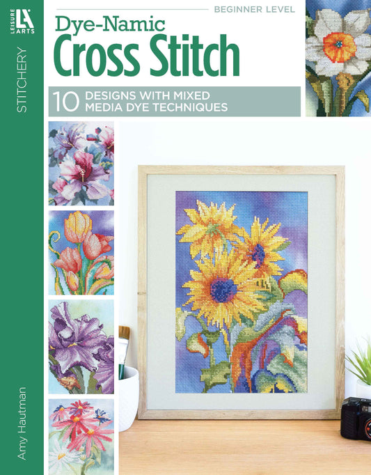 Cover of Leisure Arts' Dye-Namic Cross Stitch shows a framed sunflower pattern, nature motifs on the left, and highlights 10 mixed-media dye technique patterns for customizable Aida cloth cross stitch projects.