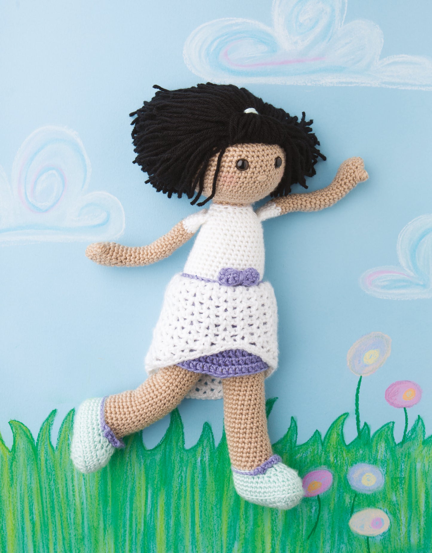 Besties—Every Girl Needs A Friend by Leisure Arts: a crocheted doll with dark yarn hair, a white and purple dress, and blue shoes, ideal for beginner doll makers, rests on a pastel scene of grass, flowers, and a cloudy blue sky.