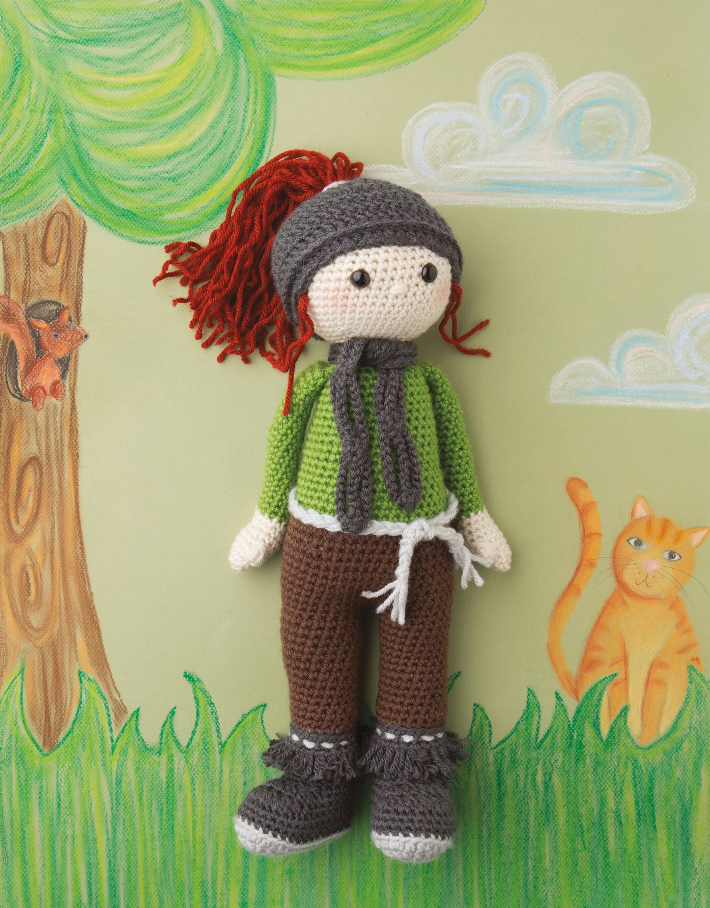 The “Besties—Every Girl Needs A Friend” crocheted doll by Leisure Arts, featuring red yarn hair and colorful clothing, stands before a playful nature scene—ideal for beginners seeking easy and charming crochet patterns.