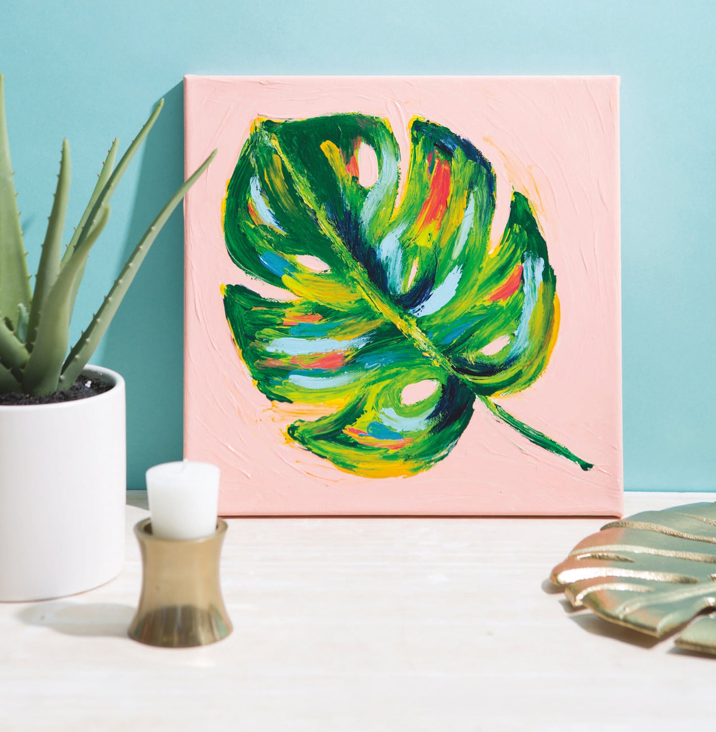 Finger Painting for Grown Ups by Leisure Arts features a colorful monstera leaf on pink canvas beside a potted succulent, ideal for beginner artists exploring modern crafts, with gold and metallic accents set against a light blue background.