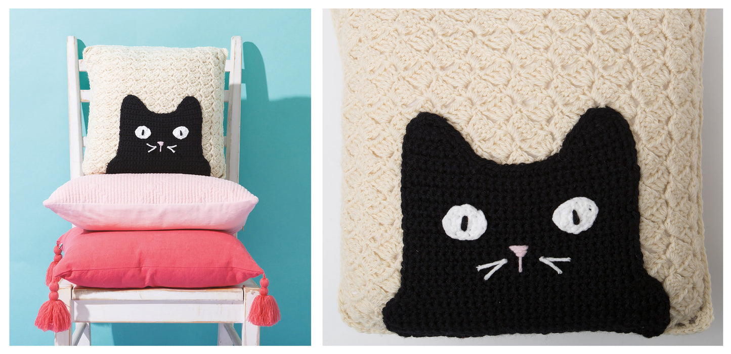 A white chair holds three pillows, with the top one featuring a crocheted black cat face from Leisure Arts’ Crochet Cool Cats Digital Download; a close-up of the cat face appears on the right.