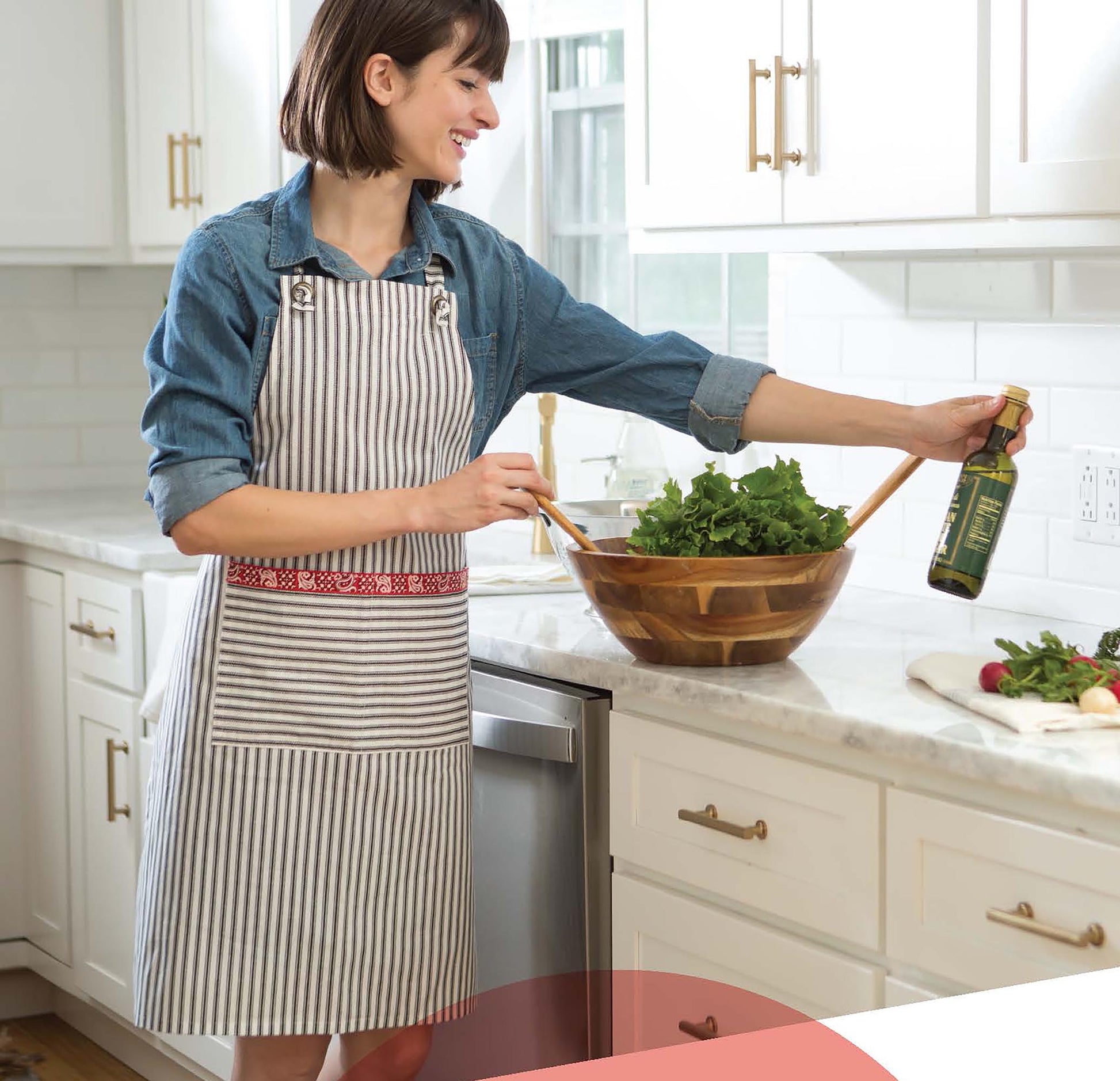 A woman in a stylish “Simple to Sew Aprons” by Leisure Arts stands in a bright kitchen, smiling as she prepares salad, showing how these aprons add flair and fun to any cooking experience. Digital download available.