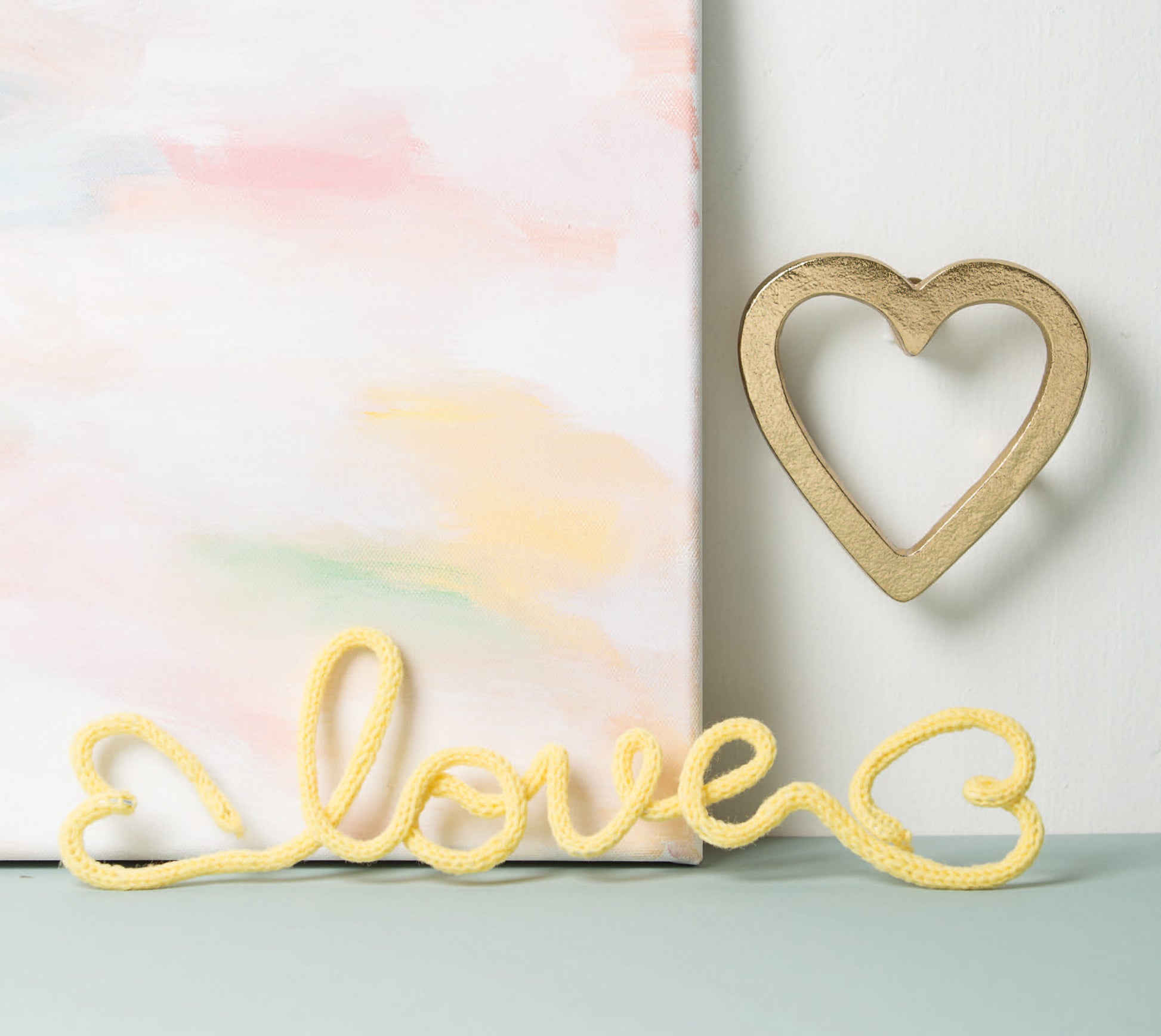 A pastel painting sits beside a gold, heart-shaped wall ornament. Up front, art wire spells “love” with hearts at each end—a charming beginner decor project from Leisure Arts’ book, Wire Crafts—18 Wire Wrapping Projects to Bend, Wrap and Twist.