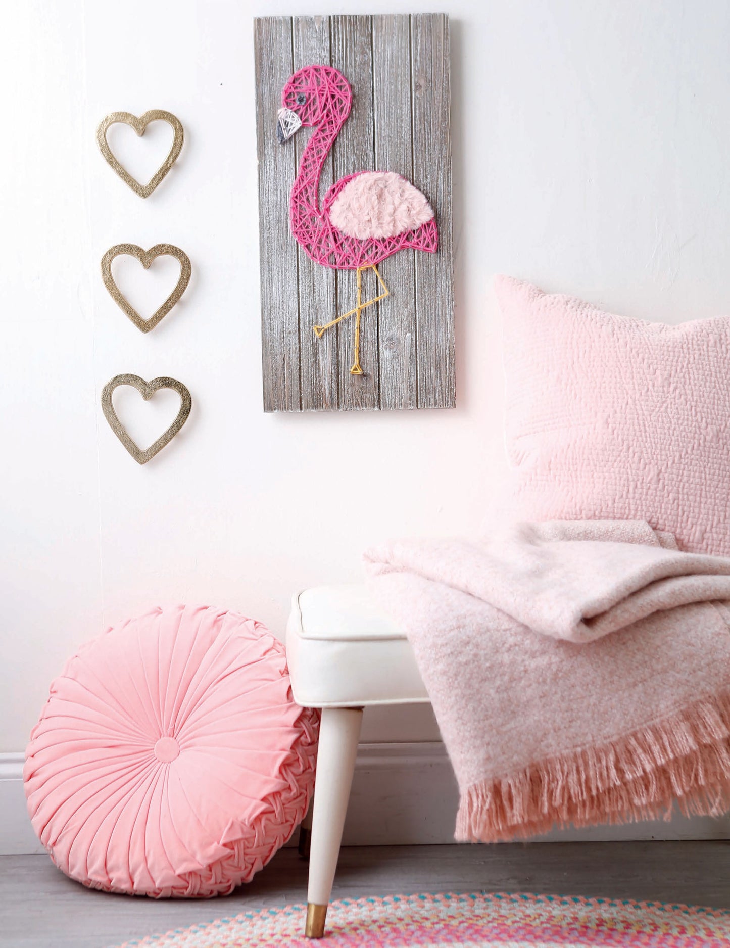 Create a cozy nook with a white bench, pink cushion and throw, round pillow, and wall art like Leisure Arts’ String Art 2—beginner string art with a flamingo—and gold heart accents, perfect inspiration for yarn and cord crafts.