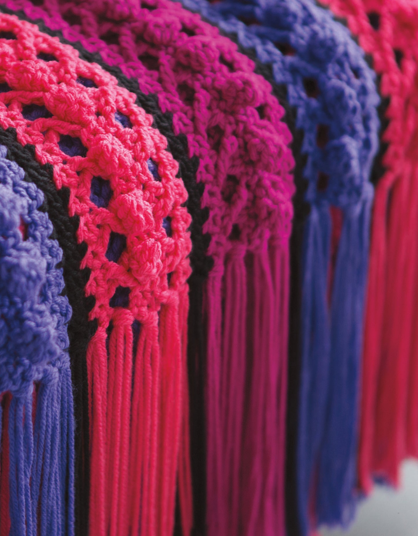 Close-up of vibrant pink and purple yarn with long fringes, featured in Leisure Arts' Bright Afghans Crochet—perfect for beginners or anyone seeking unique, colorful afghan patterns.
