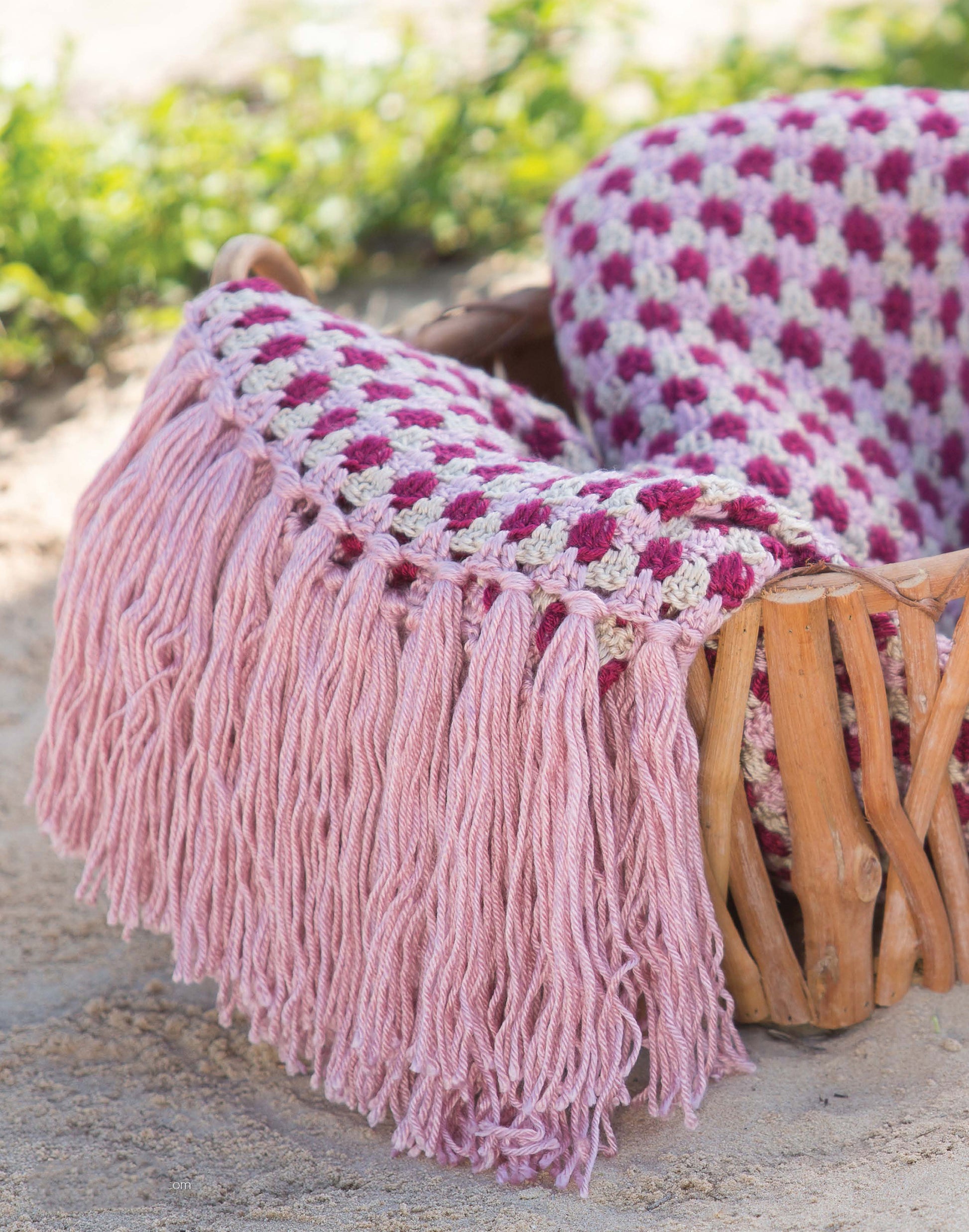 The "Restful Afghans Crochet" by Leisure Arts features a cozy, medium-weight blanket with pink and burgundy squares and thick pink fringe, shown draped over a basket—perfect inspiration for beginner crocheters.