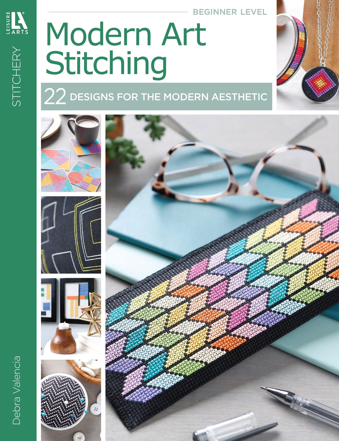 Modern Art Stitching Digital Download by Leisure Arts features 22 geometric cross-stitch projects for all skill levels on 14 count Aida, shown with eyeglasses, pen, notebook, plant, and colorful stitched items.