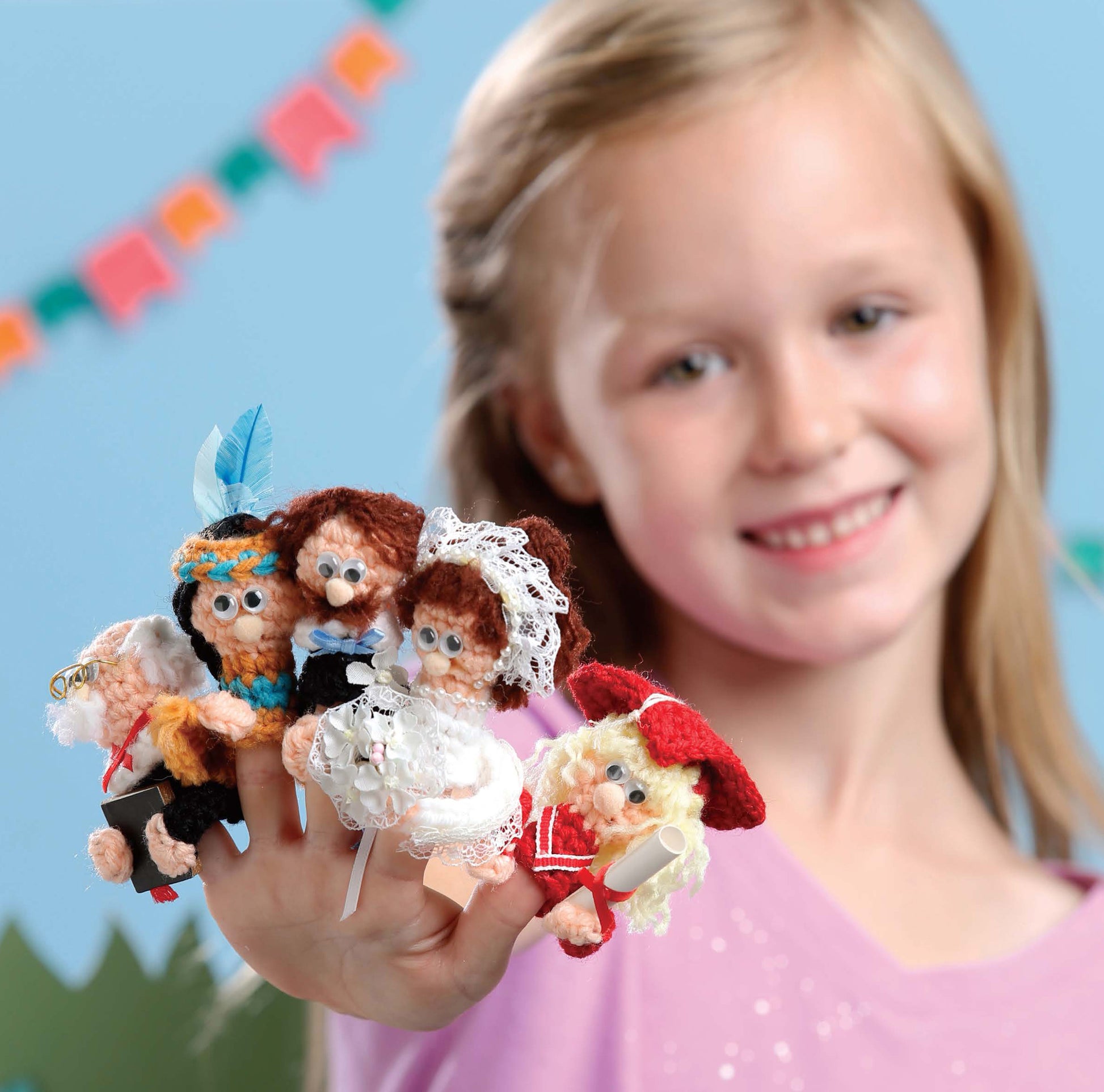 A smiling young girl shows off her hand wearing Finger Puppets Celebration from Leisure Arts, each colorful crochet puppet styled as a storybook character, set against a festive background.