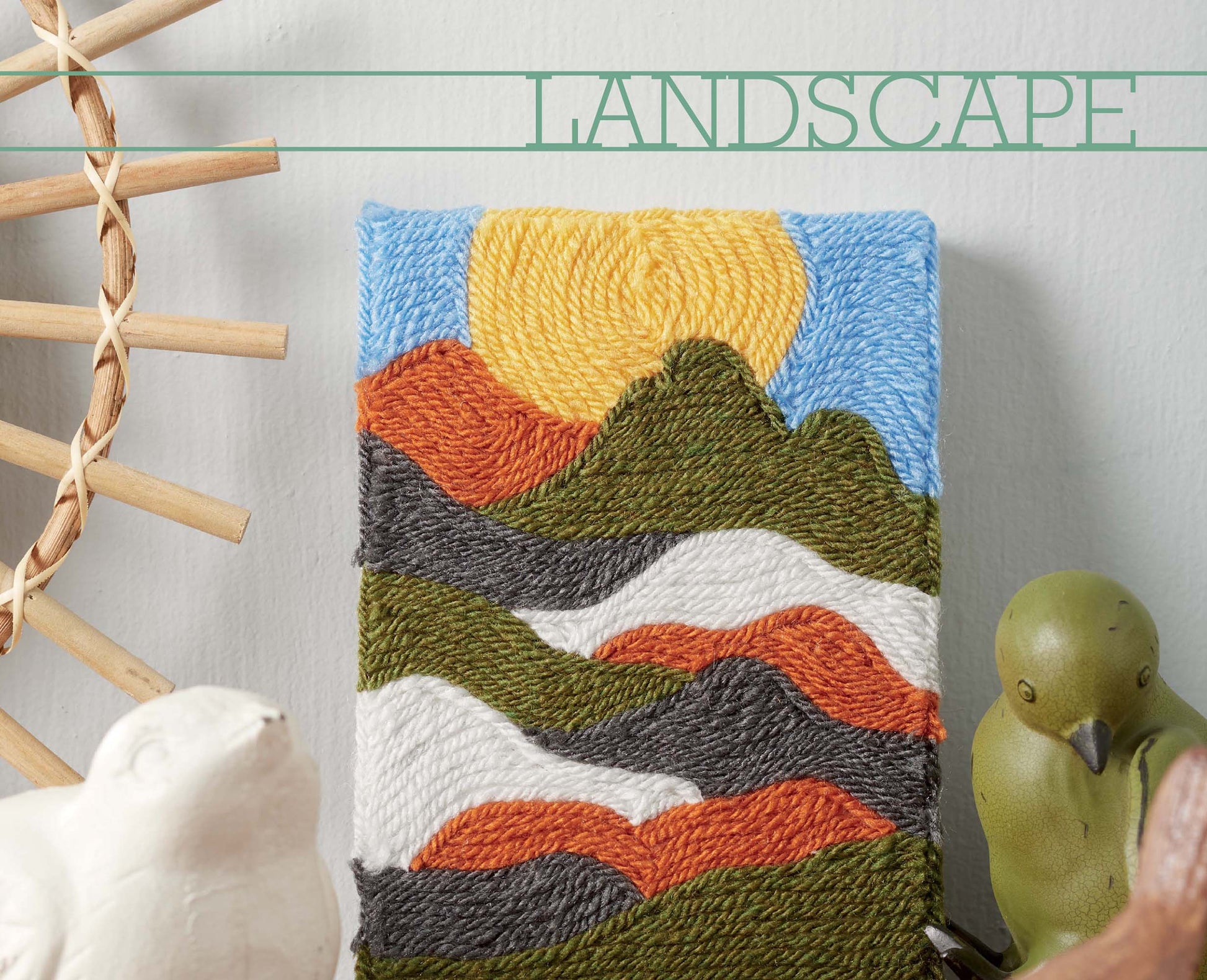 Leisure Arts’ Yarn Painting Digital Download is a beginner-friendly craft featuring a woven landscape with mountains, sun, and sky. Display upright and accessorize with bird figures, wooden sticks, and the word “LANDSCAPE” for a creative touch.