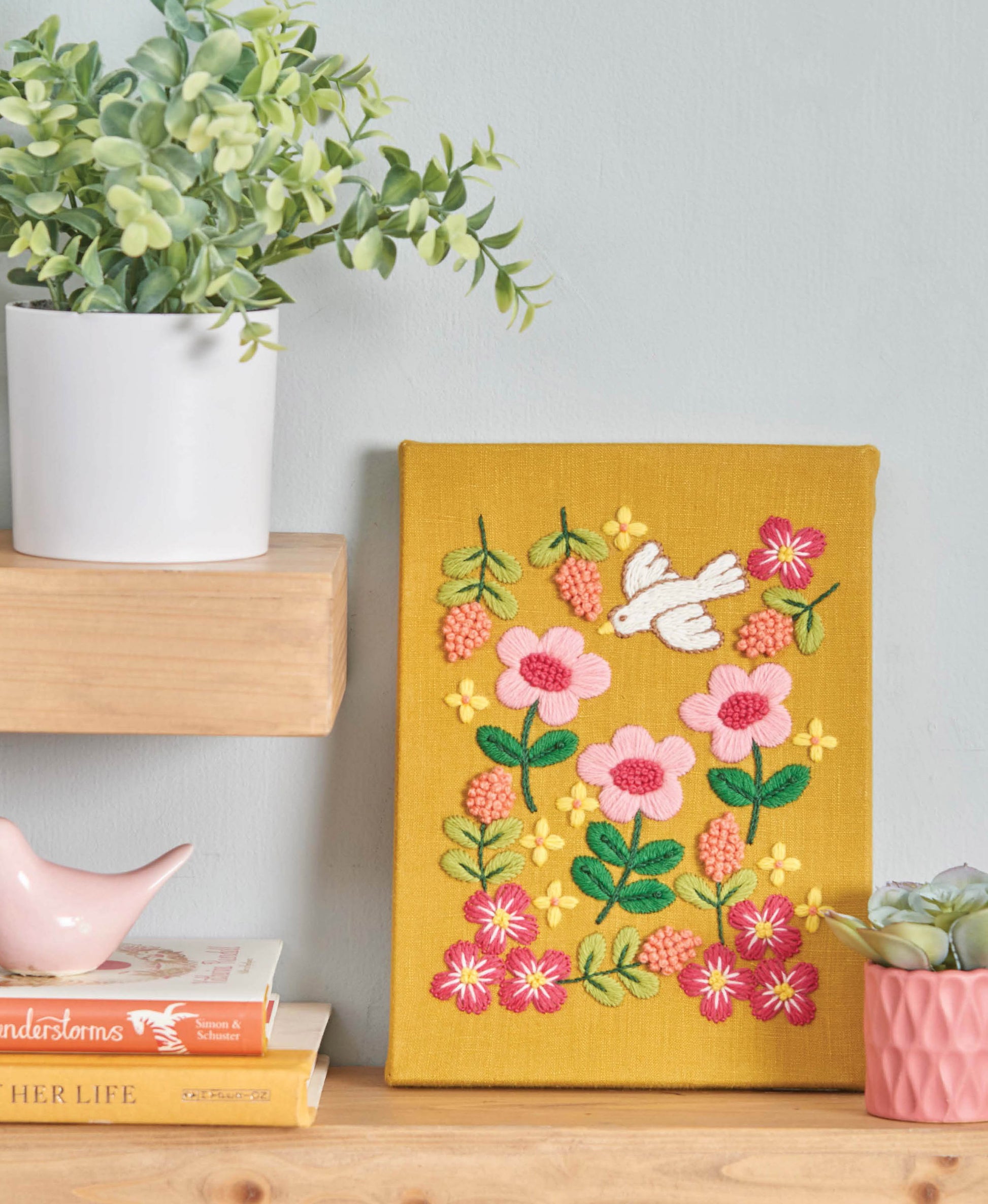 The Leisure Arts "Seasonal Embroidery—8 Projects to Complement What You Adore About Every Season" kit features a yellow canvas with pink flowers, green leaves, and a white bird—perfect for beginner to intermediate home décor craft projects.