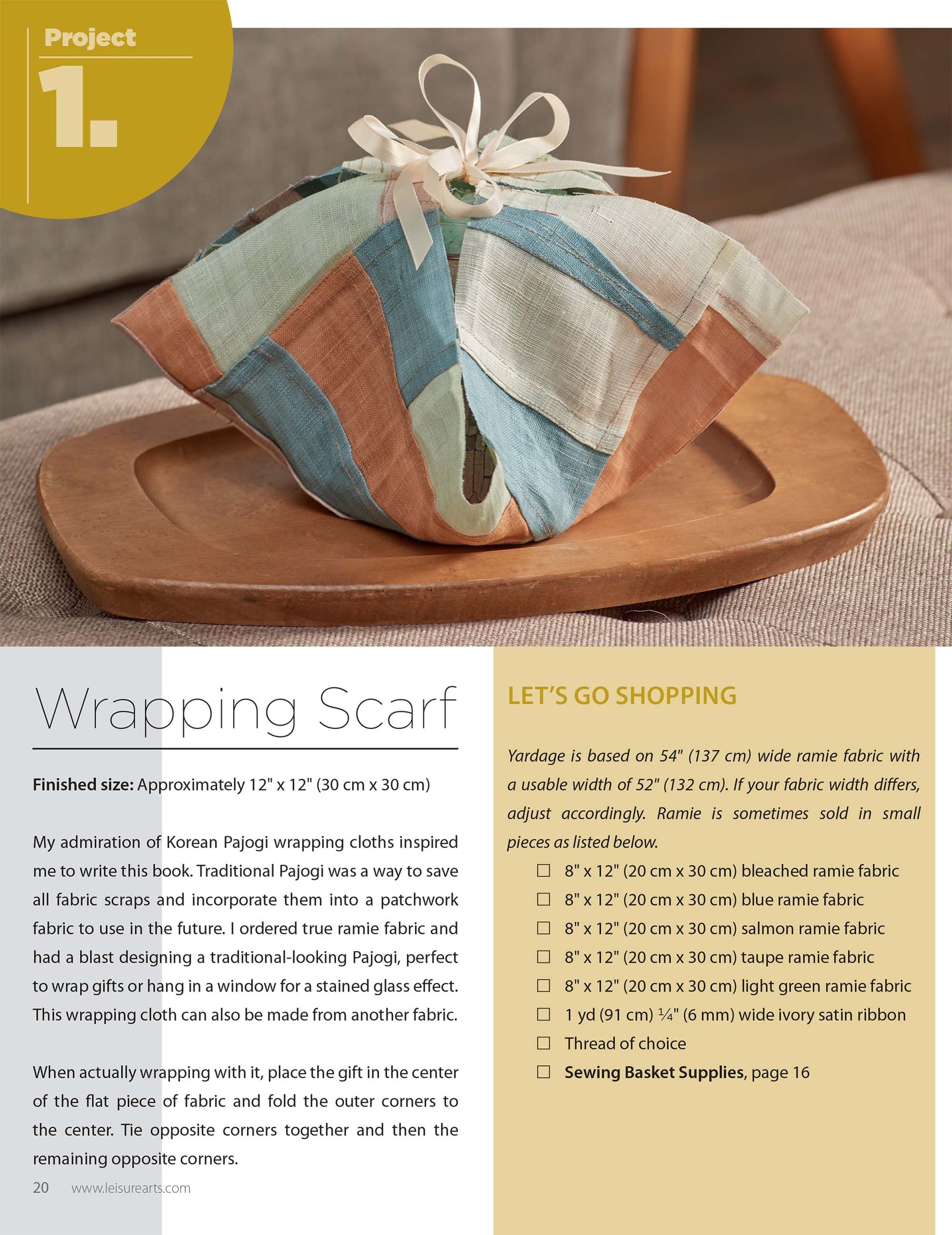 A Leisure Arts Pajogi-Style Patchworks fabric furoshiki scarf, with pastel stripes and Korean patchwork design, wraps a box on a tray. Soft lighting highlights text about a wrapping project and “Let’s Go Shopping” materials list.