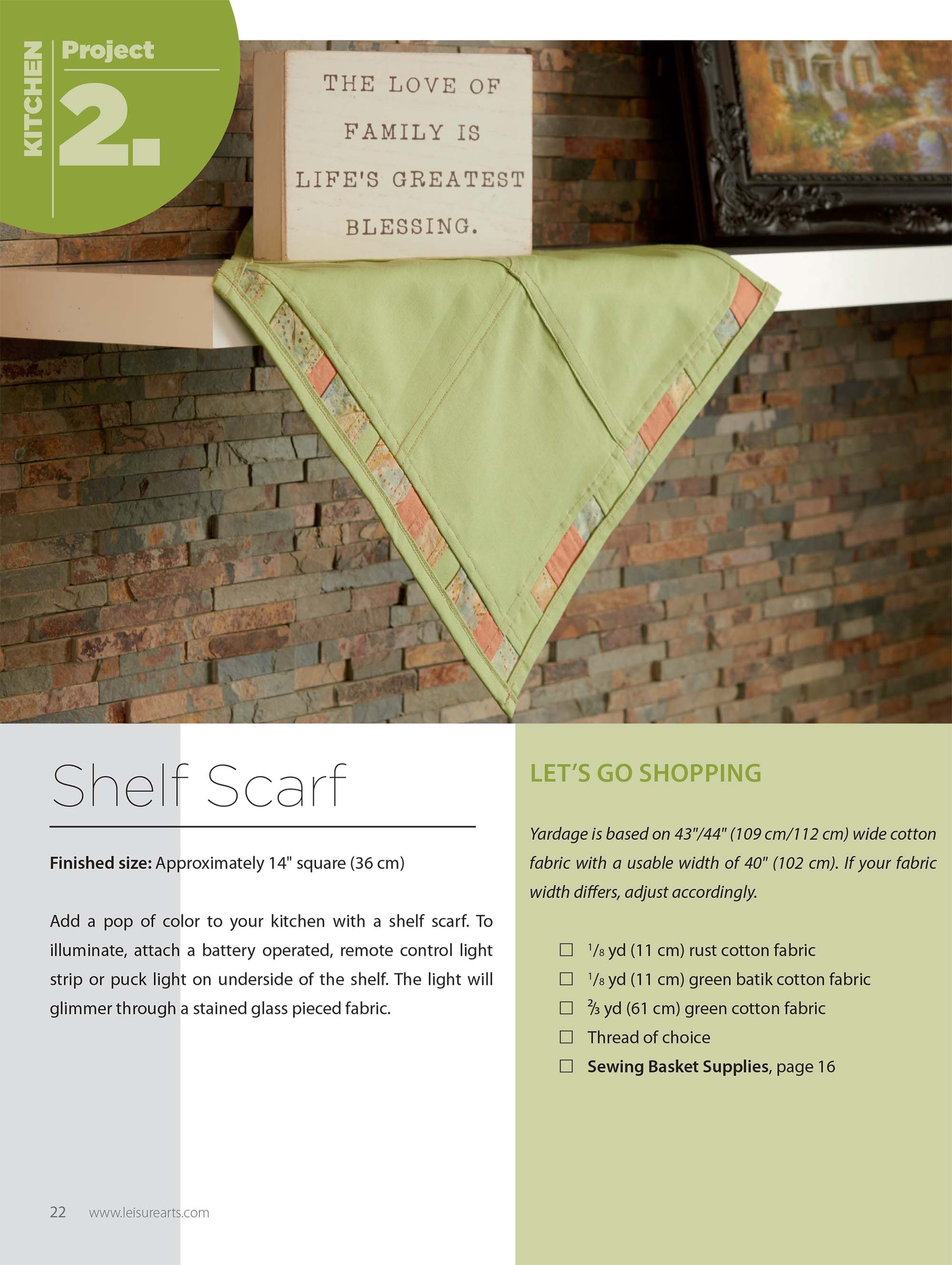 A Pajogi-Style Patchworks shelf scarf by Leisure Arts, featuring green and tan Korean patchwork with a stitched border, decorates a stone kitchen shelf. Above it is a sign reading, "The love of family is life's greatest blessing.