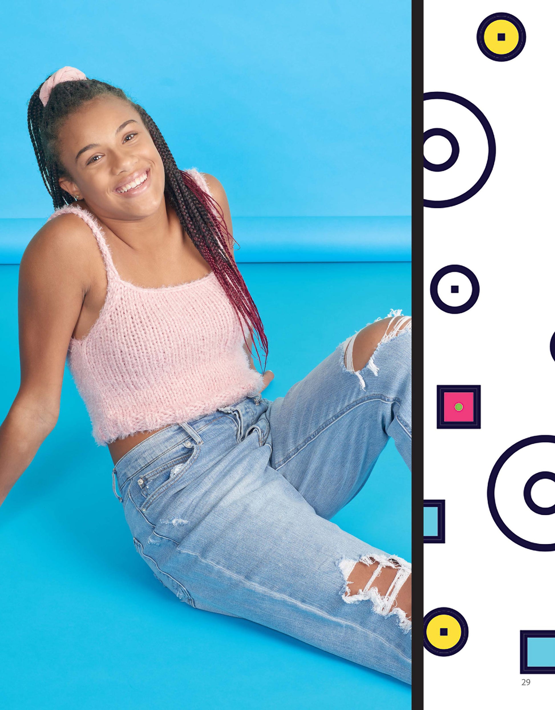 A smiling young woman with long braids, in a pink fuzzy tank and ripped jeans, sits on a bright blue floor. A white panel with geometric shapes showcases her enthusiasm for Beginner Knitting with Shayna Anne Rose by Leisure Arts.