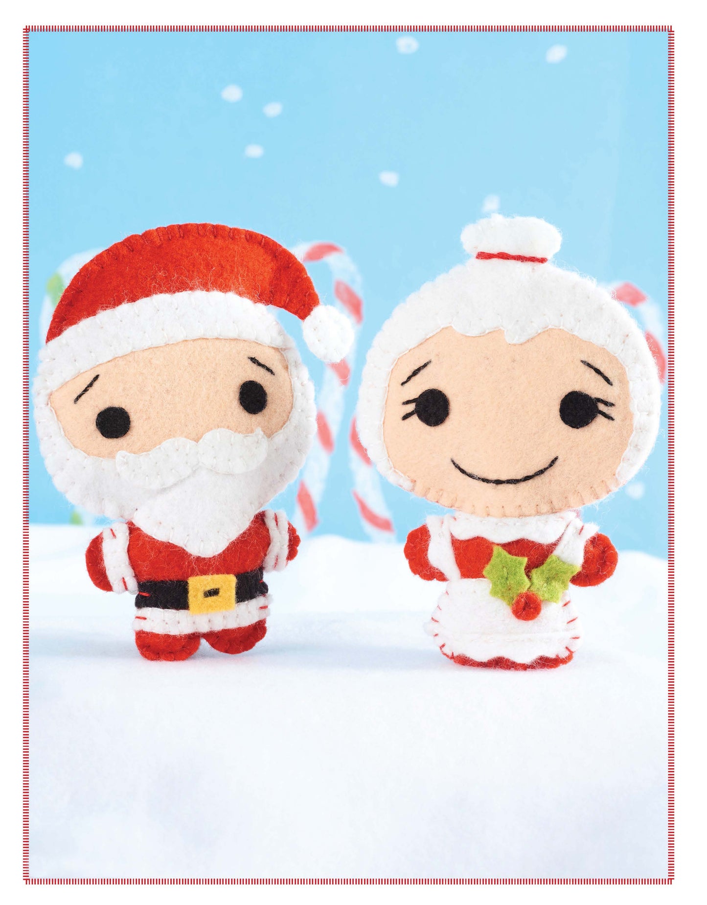 Santa's Workshop by Leisure Arts features plush felt Santa and Mrs. Claus dolls in a snowy scene with candy canes and blue sky—ideal for Christmas felt crafts or festive DIY décor. Mrs. Claus holds a holly decoration and smiles.