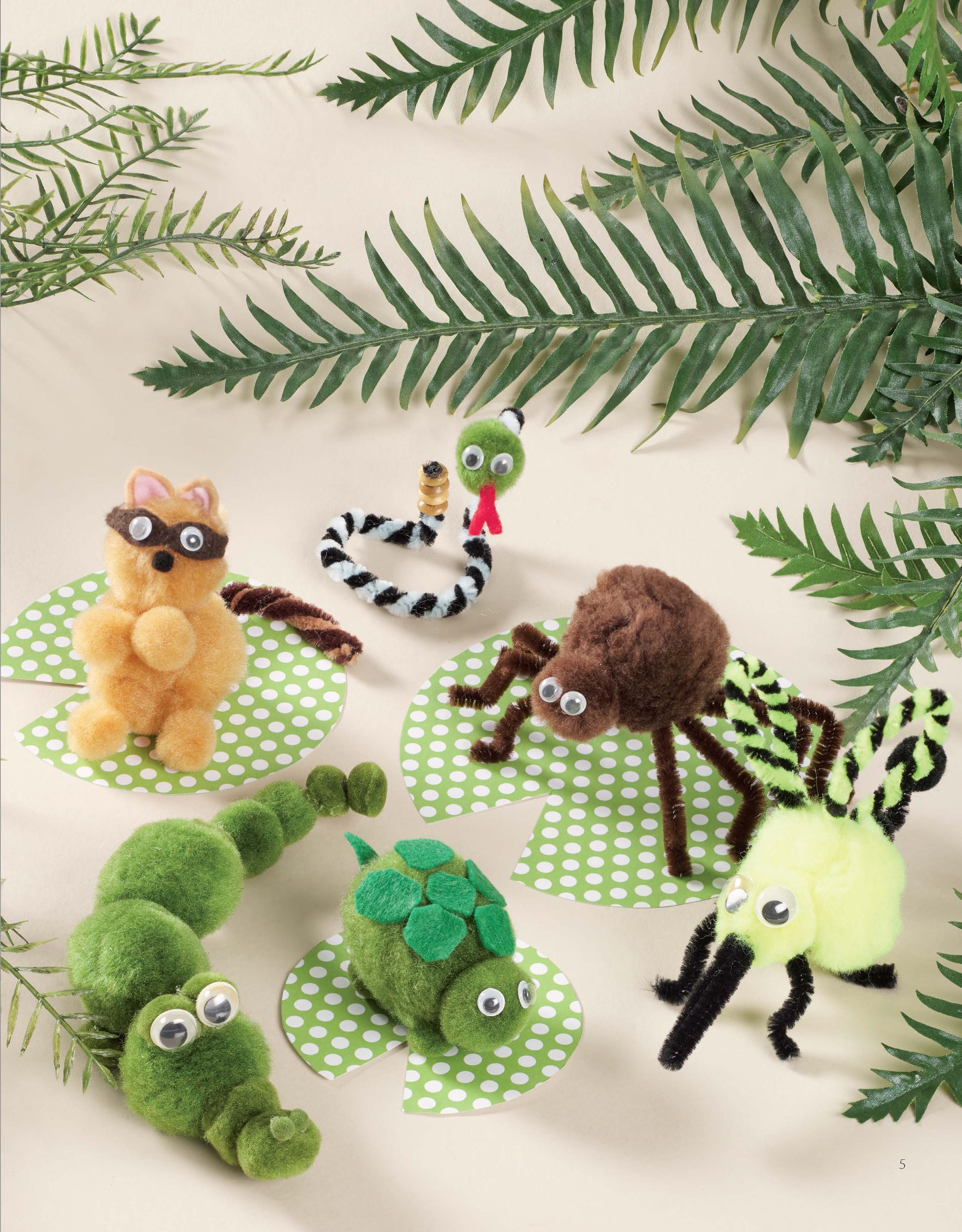 Six adorable Pom-Pom Whimsy animal and insect crafts by Leisure Arts, made from pom-poms, chenille stems, and googly eyes, are displayed on green polka-dotted circles with fern leaves on a beige background.