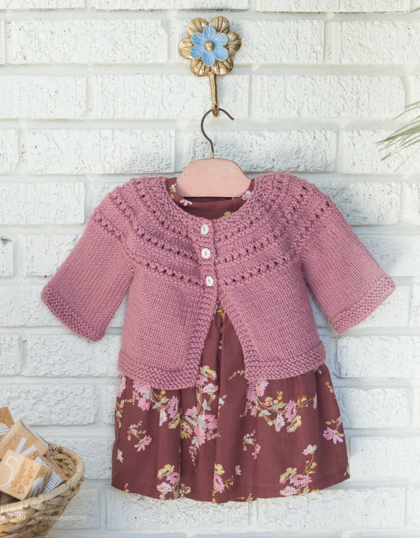 The Fashionable Lace Digital Download by Leisure Arts is displayed hanging on a decorative flower-shaped wall hook against a white brick wall over a brown floral dress.