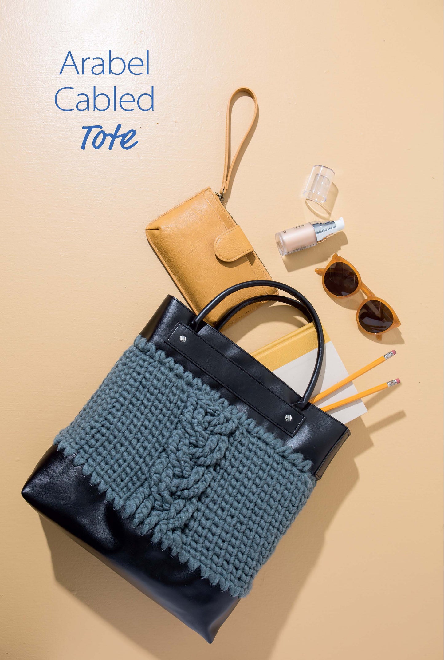A black tote bag with a blue cabled knit front sits on a beige surface surrounded by accessories. Text: Discover stylish designs in Crochet Handcrafted Handbags Book 3 Digital Download from Leisure Arts.